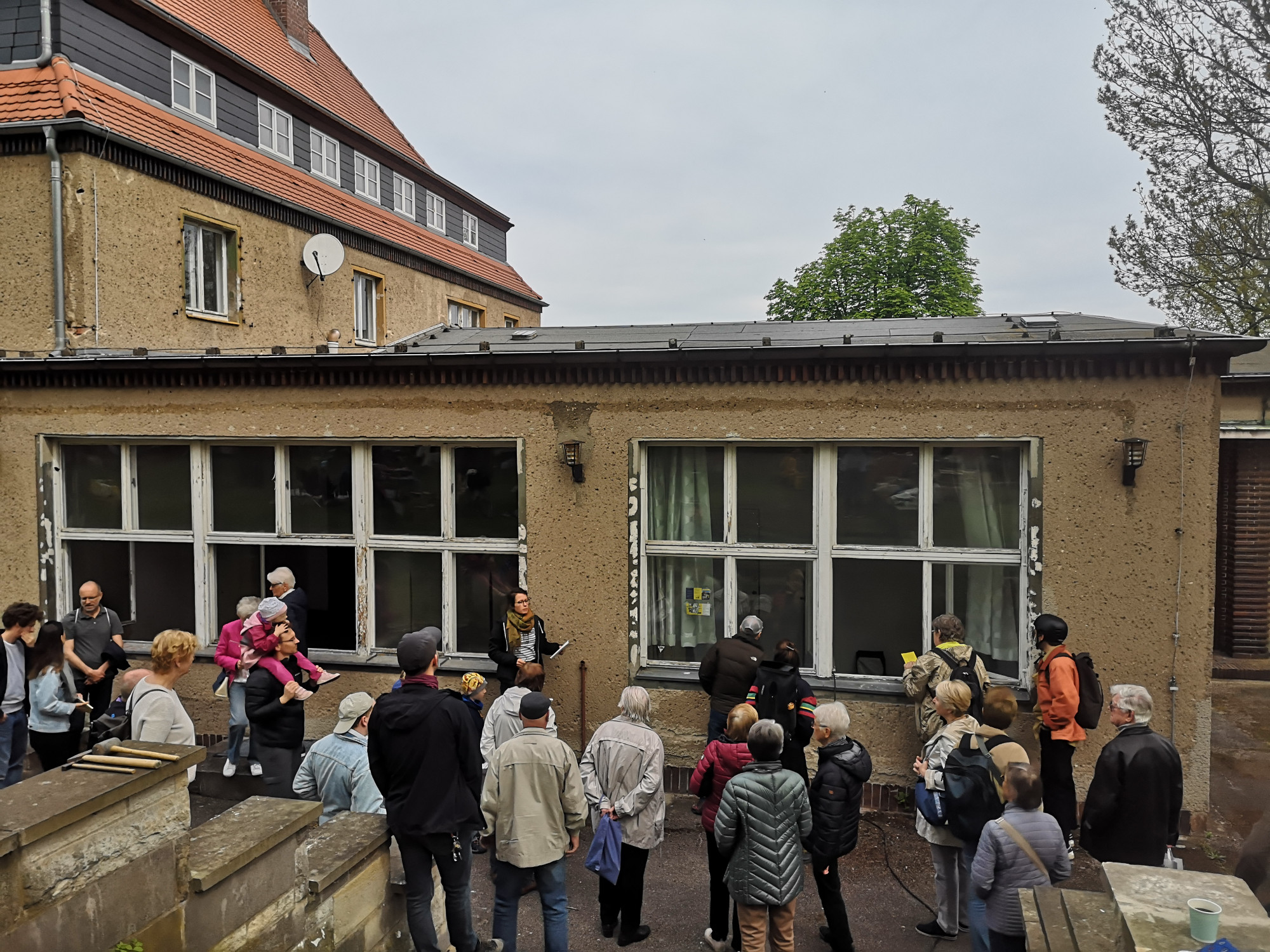 Eine Gruppe steht vor einem alten Arbeiterkulturhaus und betrachtet die große Fensterfront.