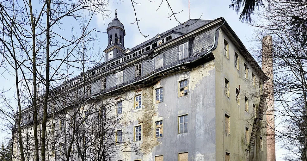 großes Haus mit spitzem Turm und grauem Schieferdach aus einer untersichtigen Perspektive fotografiert