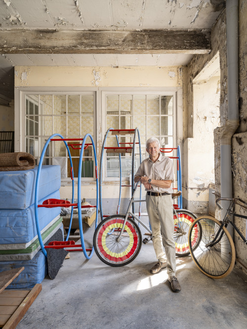 Mann steht vor einem Fahrrad mit bunten Rädern in einer alten Spinnmühle