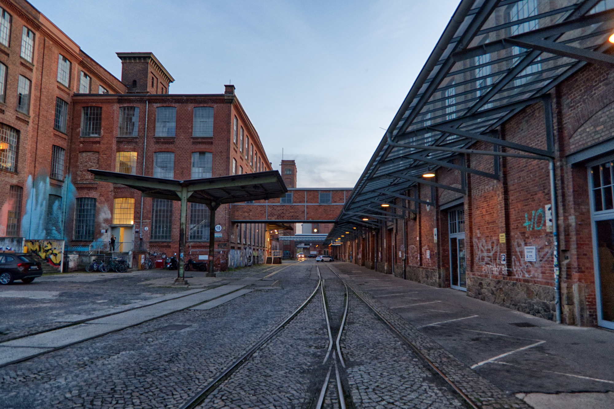 Es ist der Innenhof einer alten Fabrikanlage mit Bahnschienen in der Mitte zu sehen.